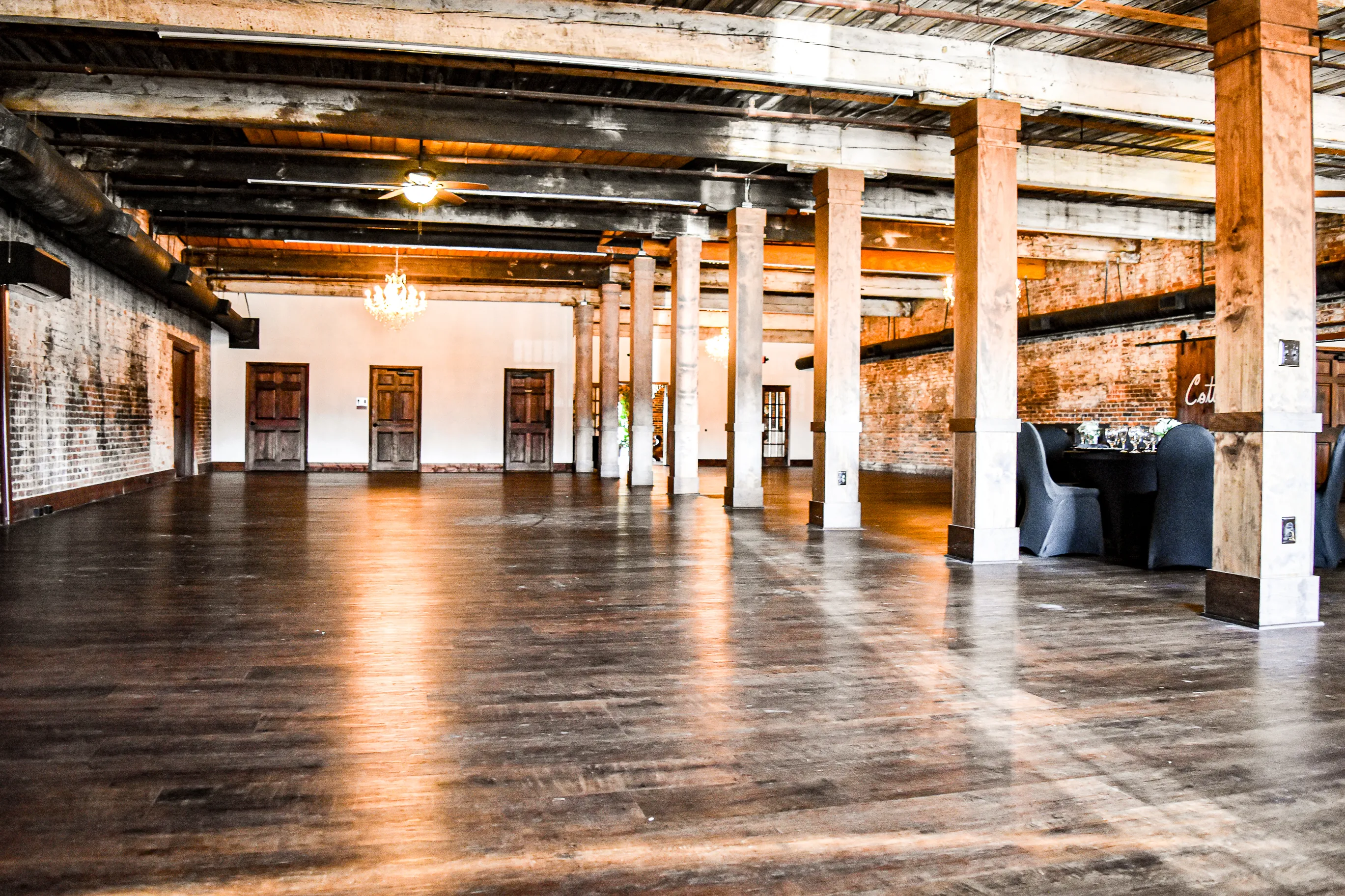 The Cotton Loft event room empty, showing its long wood floor, timber columns, brick walls, and chandeliers