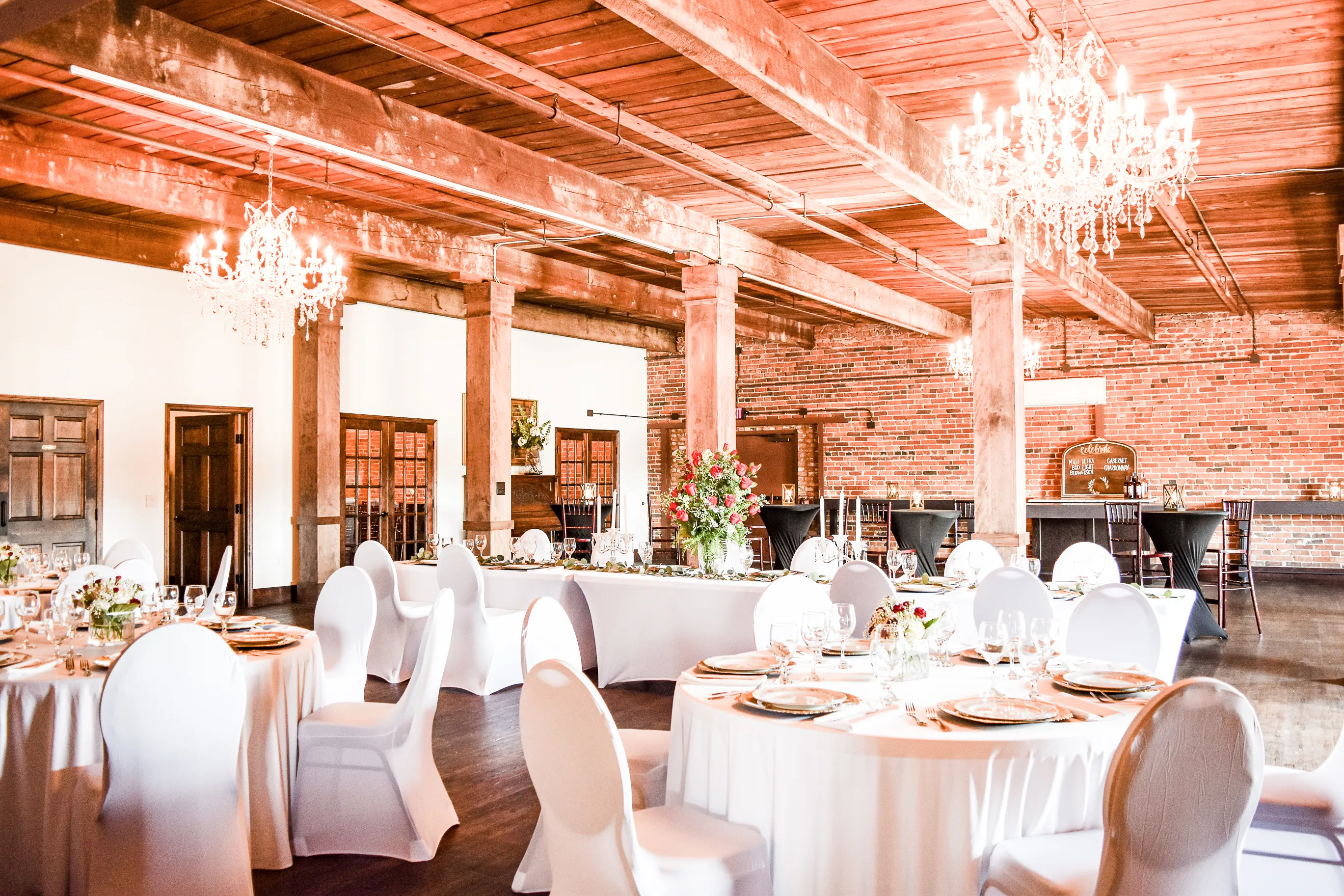 The Cotton Loft arranged for a reception with white-clothed tables beneath timber beams and chandeliers